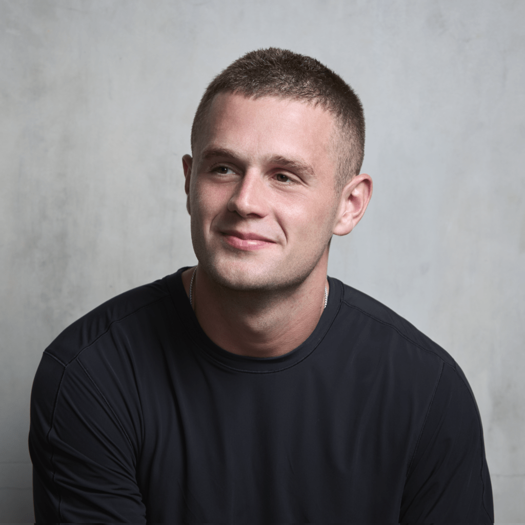 A young man with short hair smiling against a gray backdrop, wearing a black shirt.